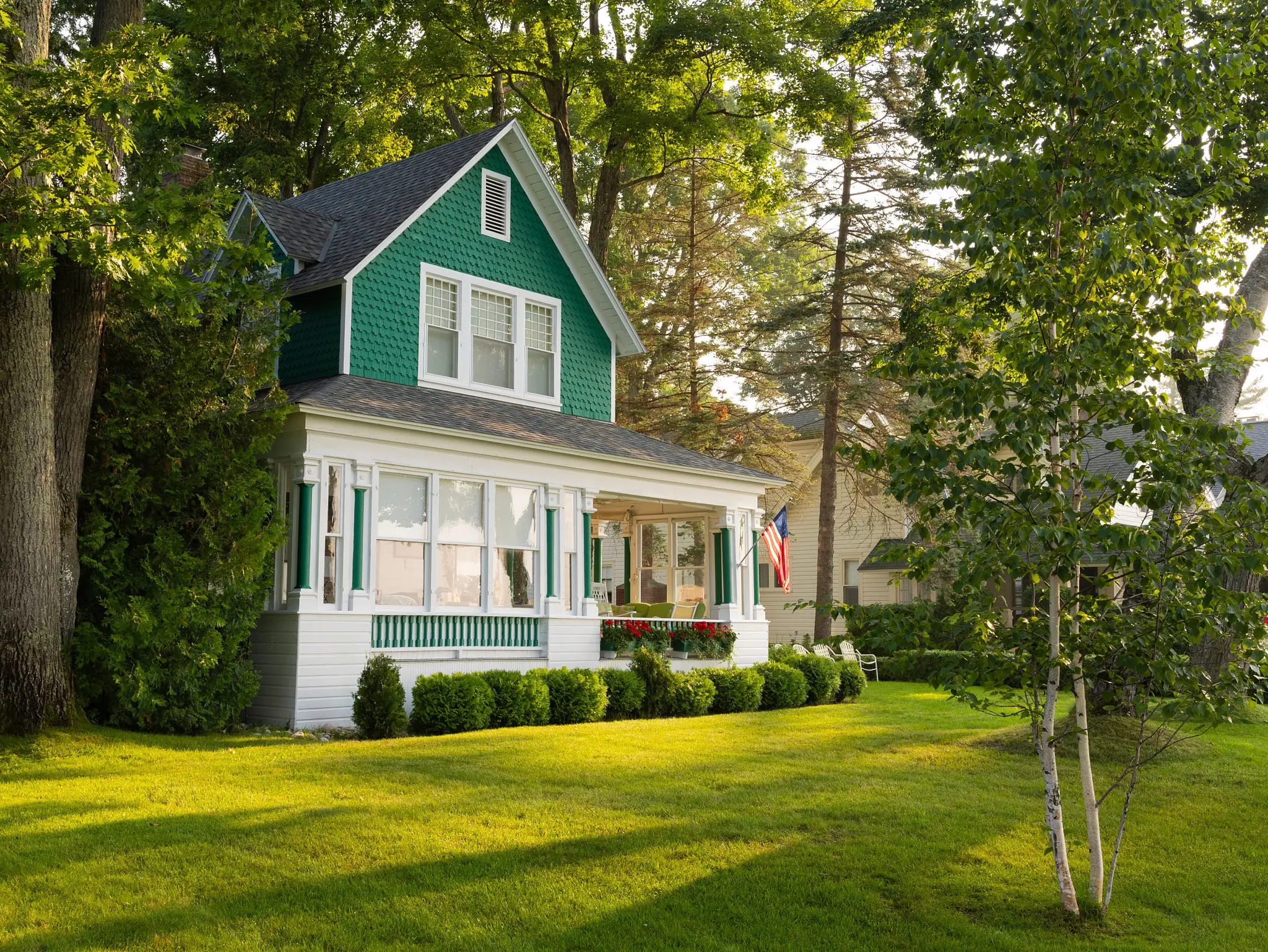 Charming green house with a spacious porch surrounded by lush trees.
