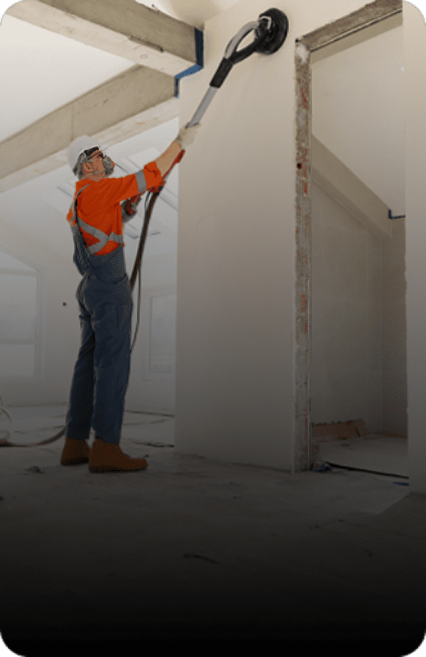 Worker sanding a white wall indoors.
