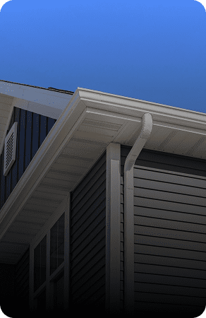 Close-up of a house roof with gutter and downspout against a clear blue sky.
